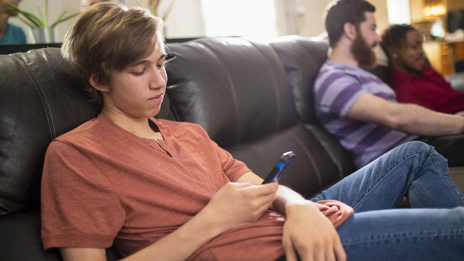 A young man looking at his phone seated on a couch.