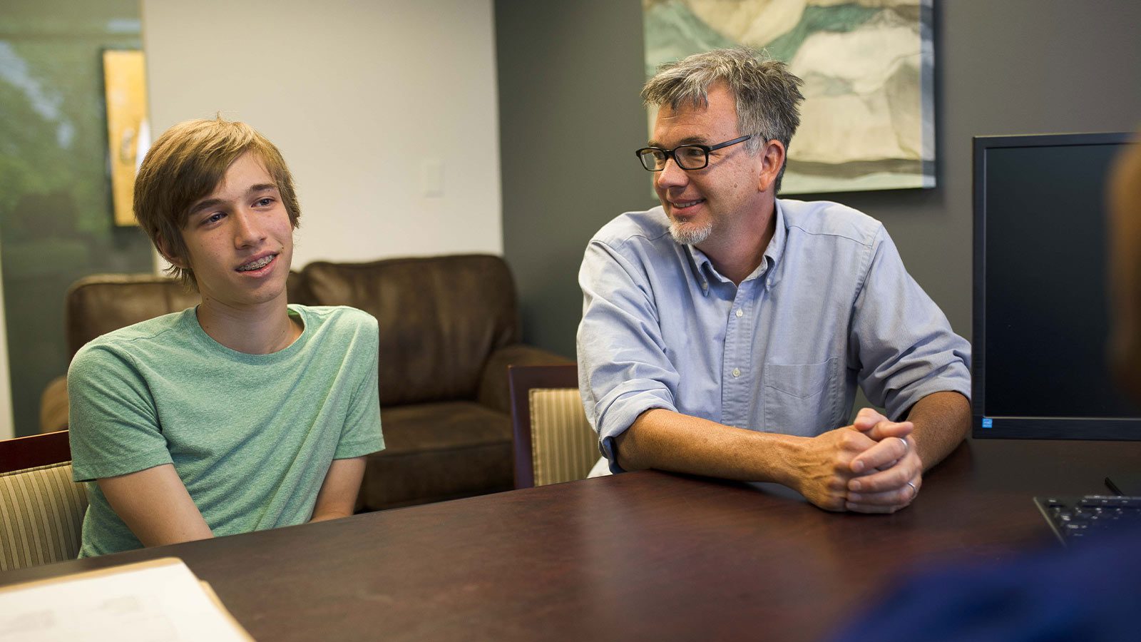 A father and son having a discussion at a desk with an admissions coordinator.