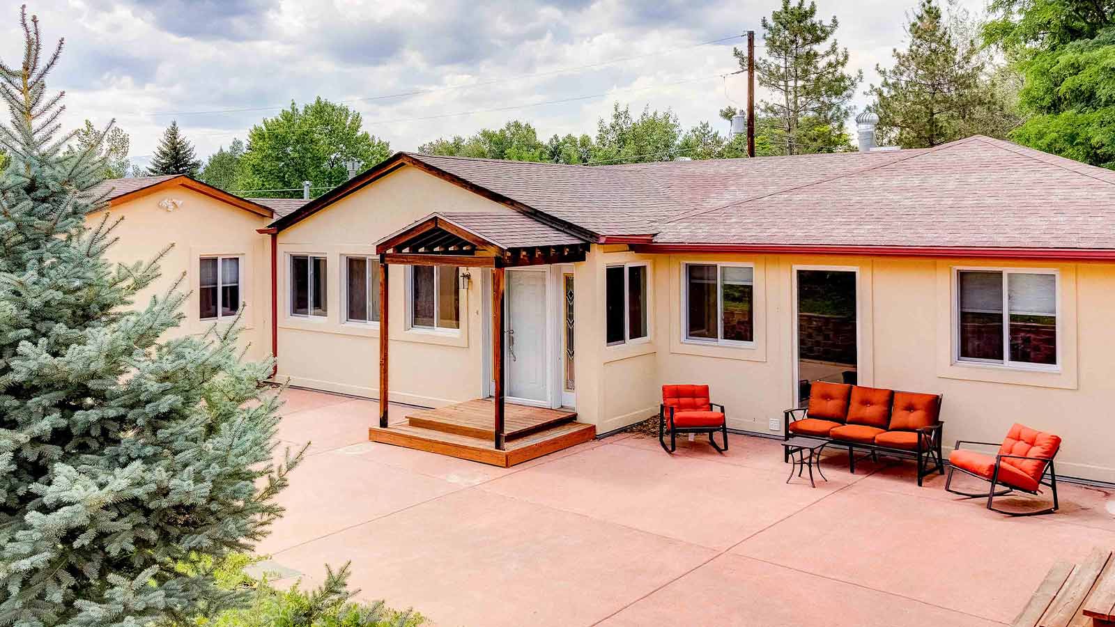 An home exterior with a modern covered porch and outdoor seating area, set against evergreen trees.