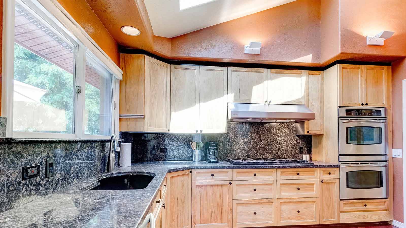 A sunny kitchen corner featuring natural wood cabinets and black granite countertops.