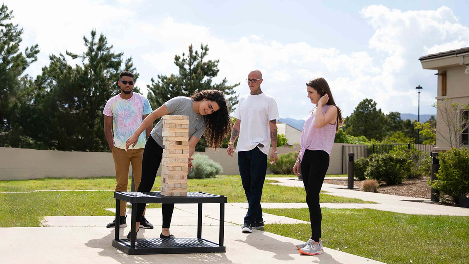 Four people, two men and two women, are playing a giant game of Jenga outside on a sunny day.