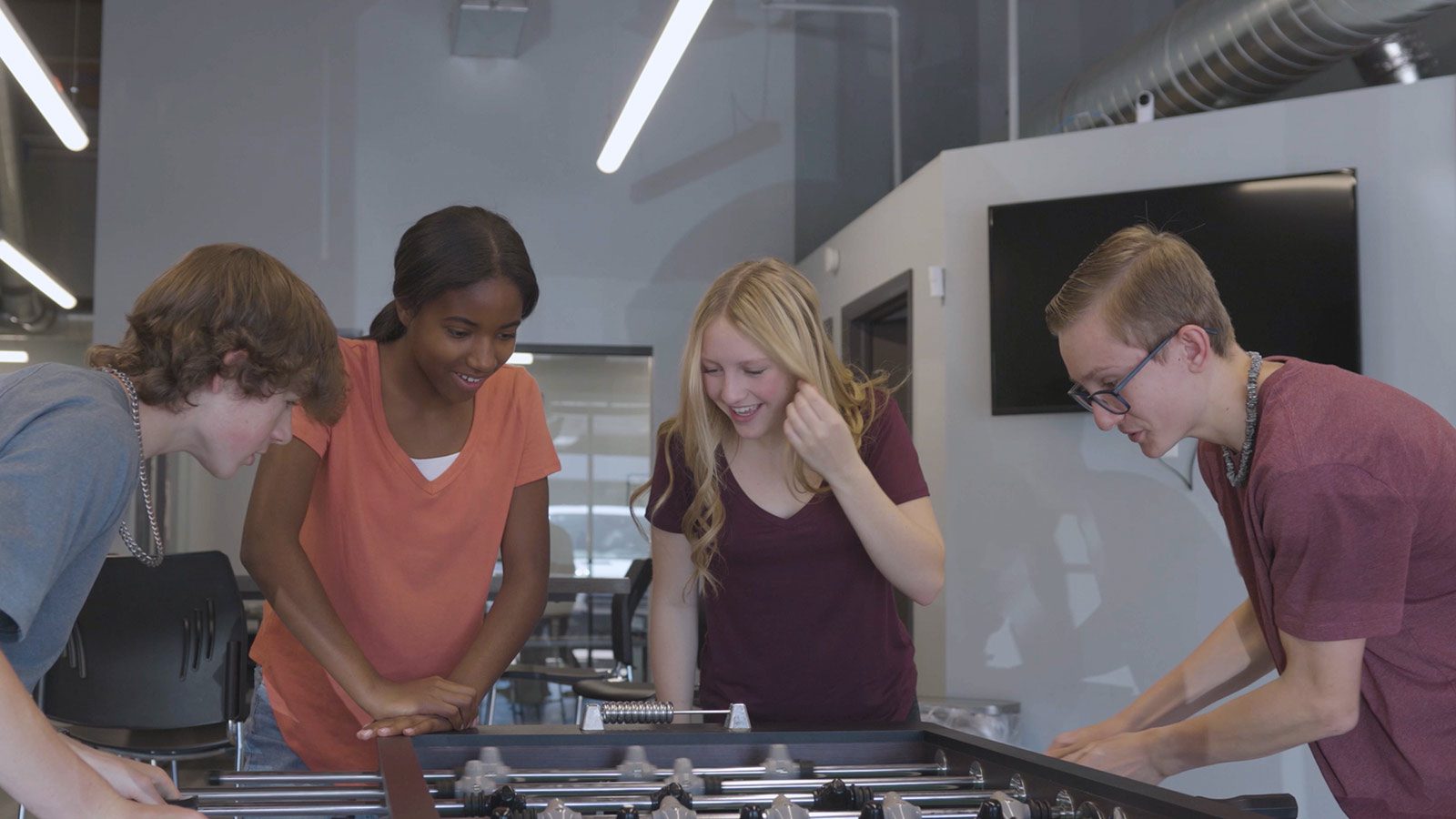 Teenagers enjoying a game of foosball in a bright, open space at a mental health center.