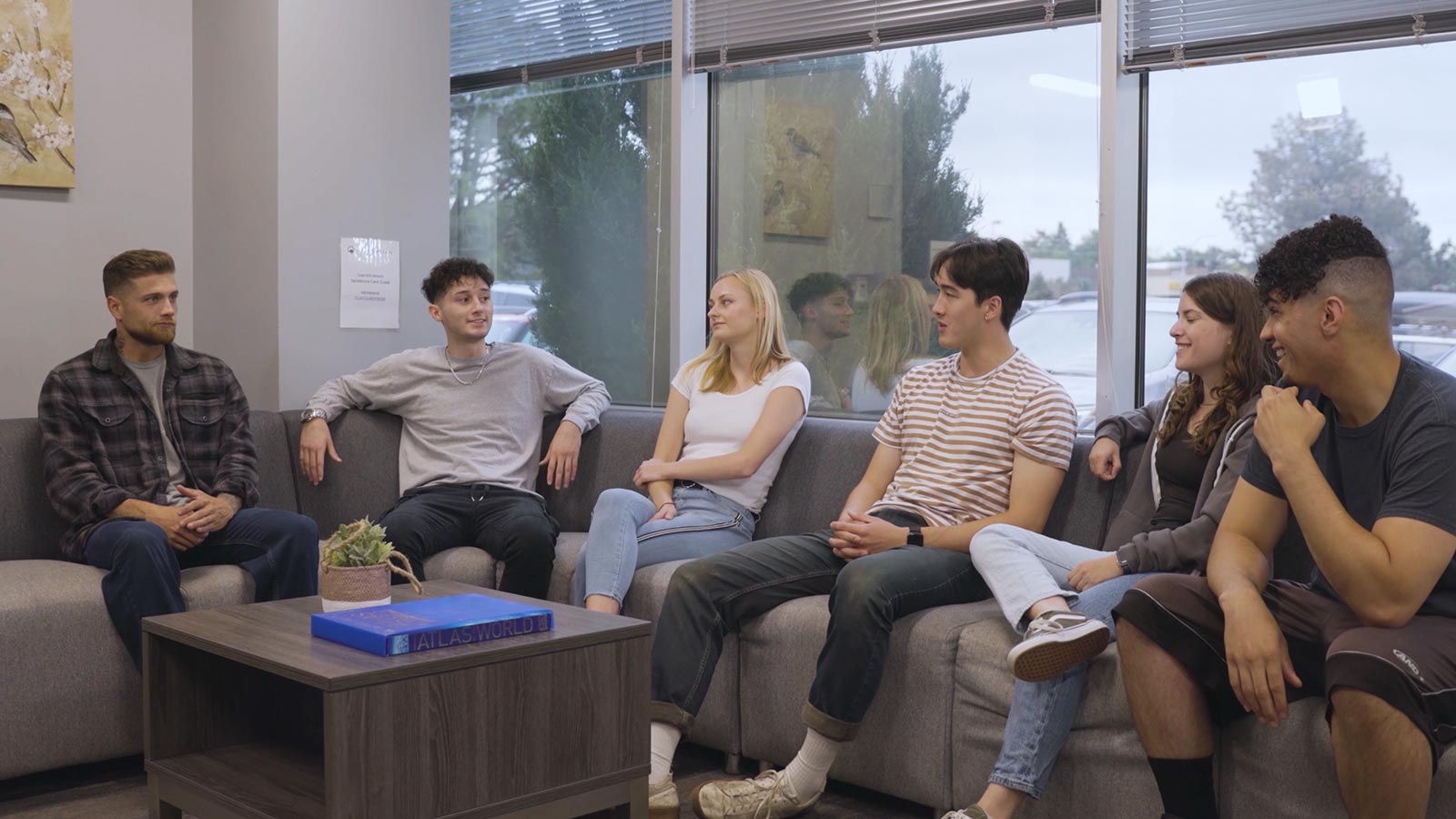 A relaxed social scene in a modern waiting area with a group of young adults having conversations.