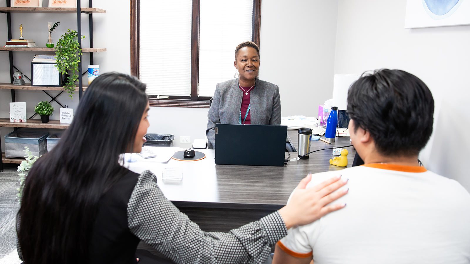 A counseling environment with a counselor and two clients having a discussion across a desk.