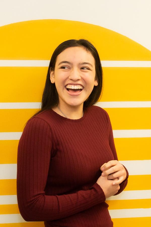 A teenage girl with long hair laughing against a mural.