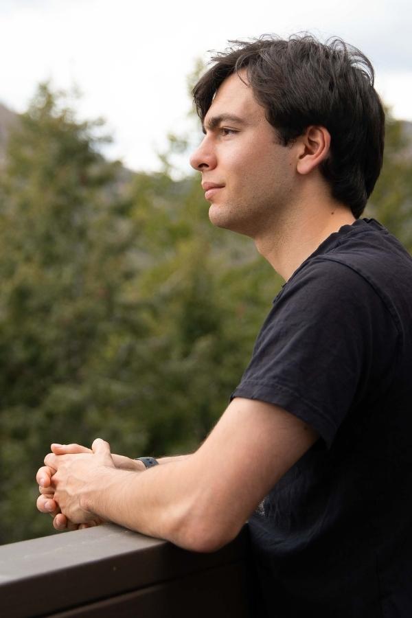 A young man with his hands folded looking out at the forest.