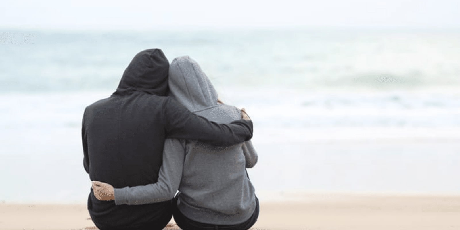 Couples wearing hoodies hugging each other on a beach