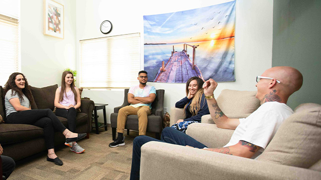 A group of people sit relaxed in a well-lit living room, engaging in a cheerful conversation.