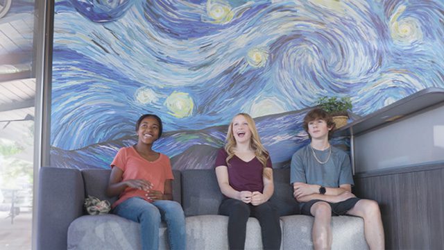 Three teenagers are seated on a couch in a lobby with a large Van Gogh-inspired mural and the Sandstone Care logo in the background.