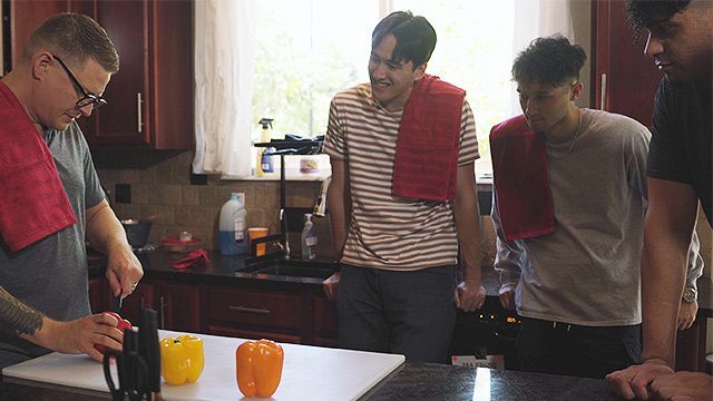 Three young men enjoy a culinary lesson together in a kitchen setting.