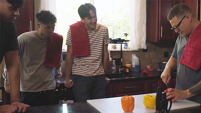 Three young men enjoy a culinary lesson together in a kitchen setting.