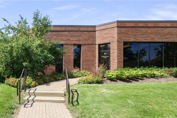 A brick office building with reflective windows and a landscaped entrance with flowers and shrubs.