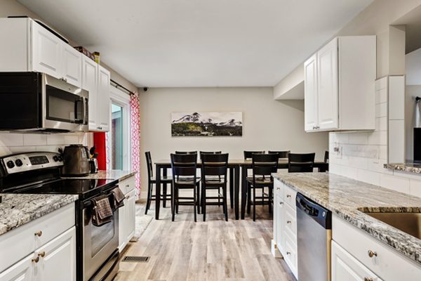 Sandstone Cares Colorado Springs Transitional Livings modern kitchen with white cabinetry, stainless steel appliances, and a dining area with a black table set.