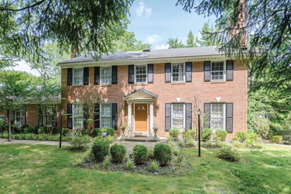 A classic two-story brick house with white trim and a landscaped front yard.