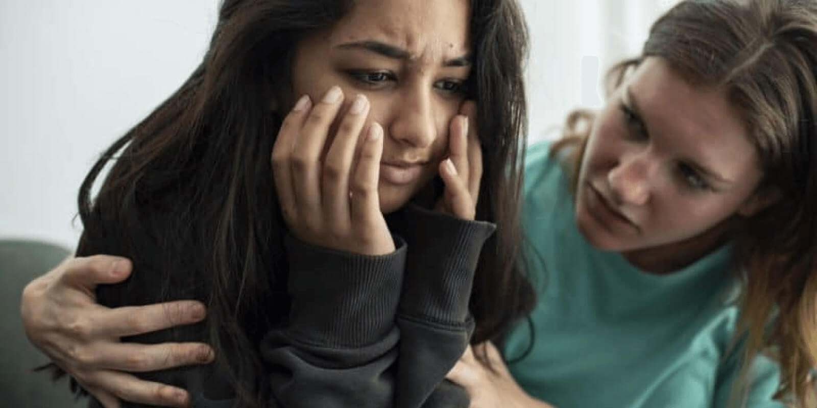 A teen girl looking sad while her friend consoles her