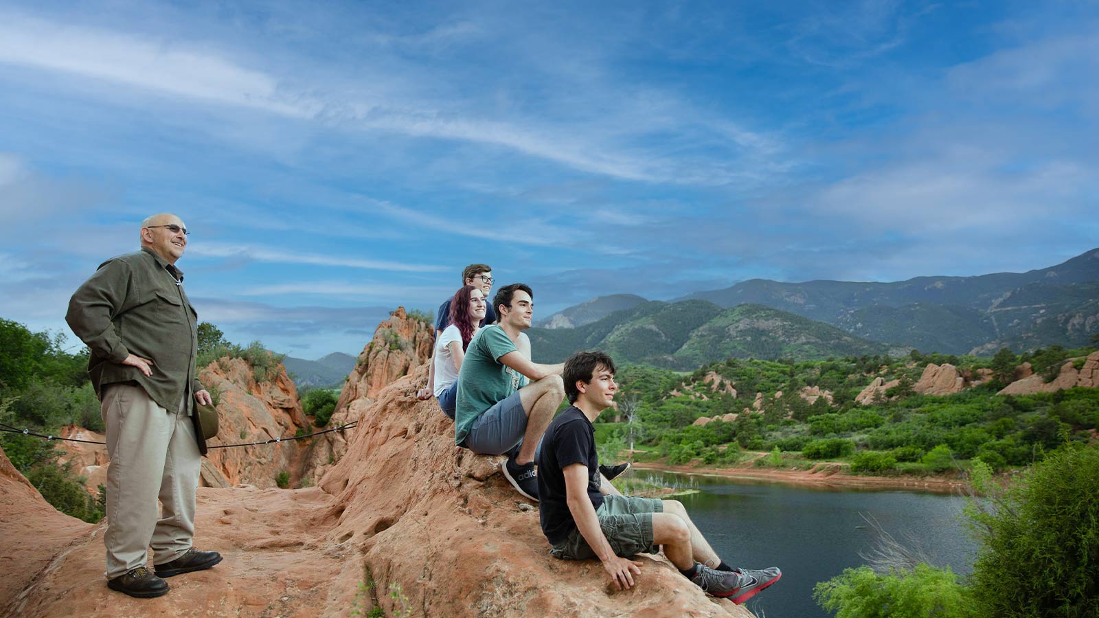 several people sitting on a rock overlooking a lake and mountains