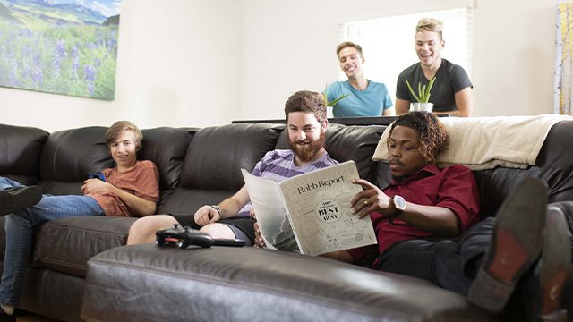 Friends share a lighthearted moment on a large couch, reading a newspaper together.
