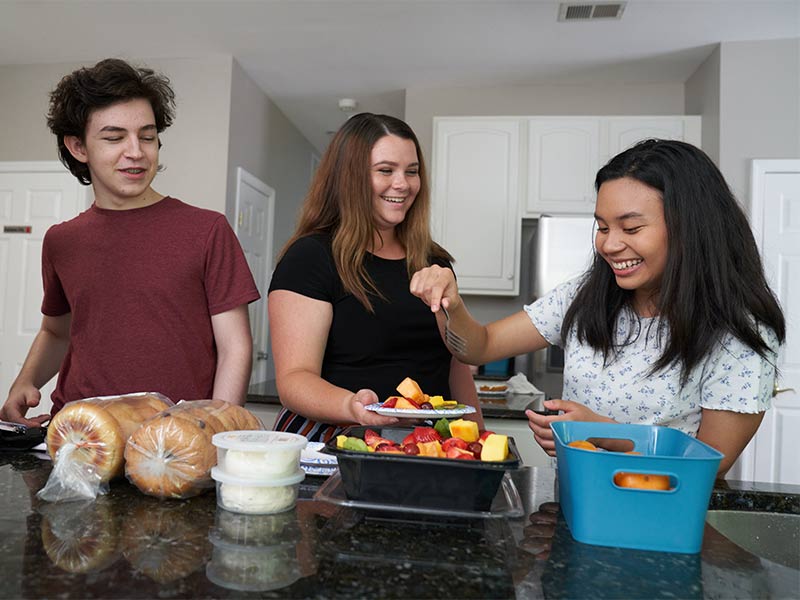 three people standing around a kitchen counter with food on it