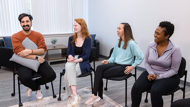 Four individuals seated in a group therapy circle, smiling and interacting.