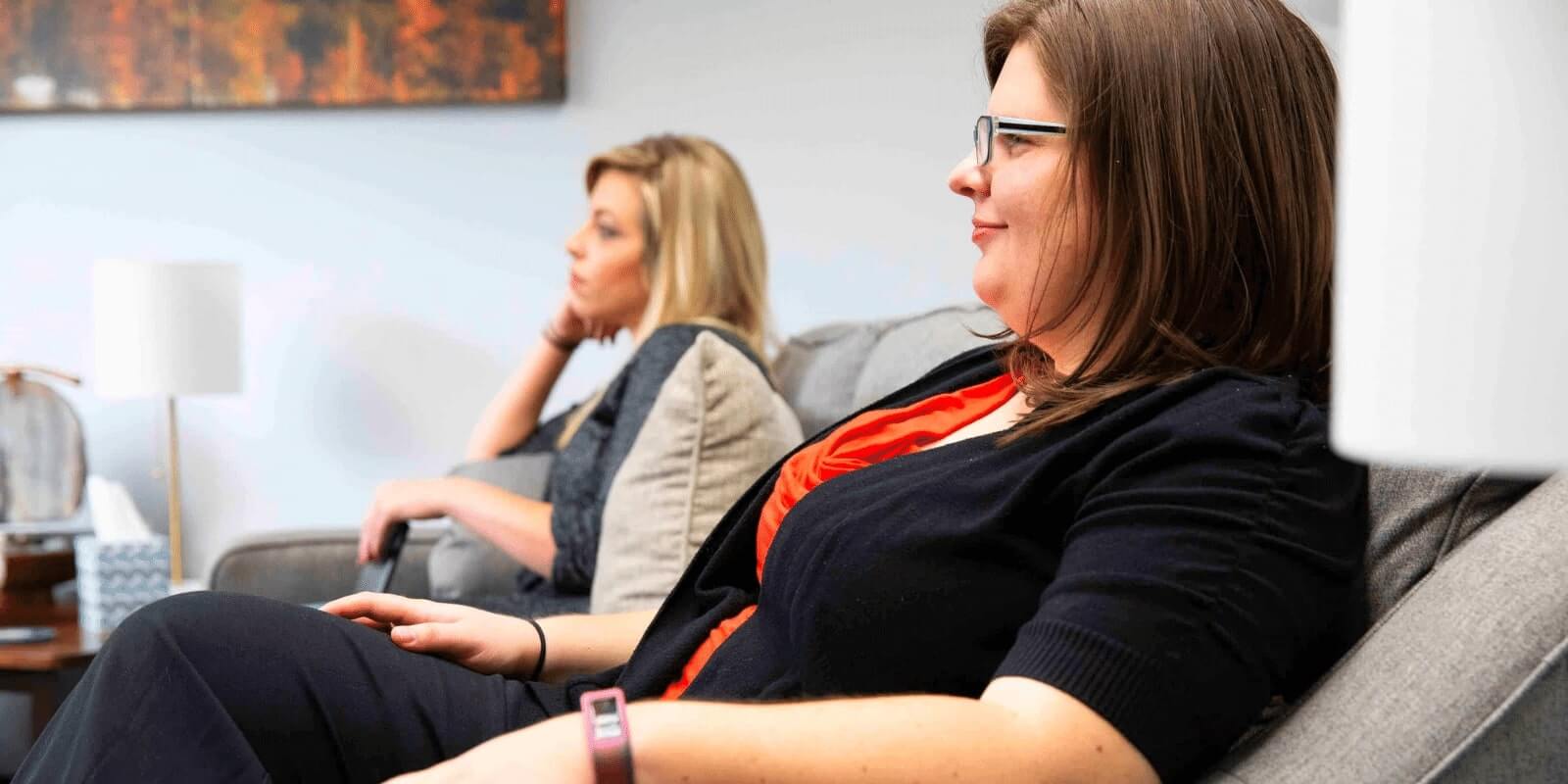 Two moms sitting on the couch smiling at something