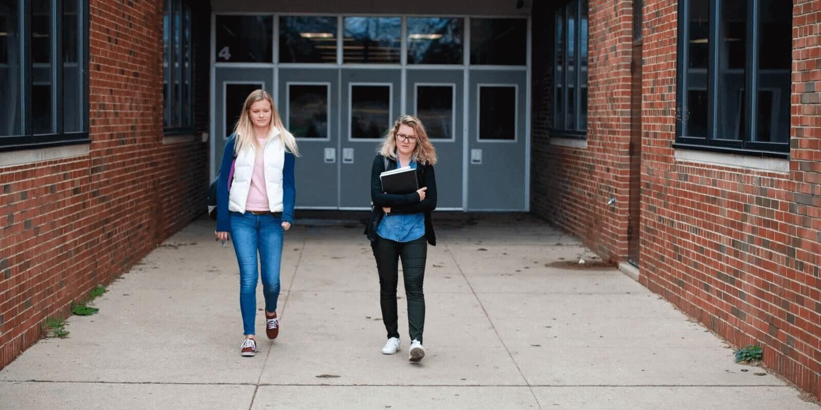 Two high school girls walking outside the main school entrance