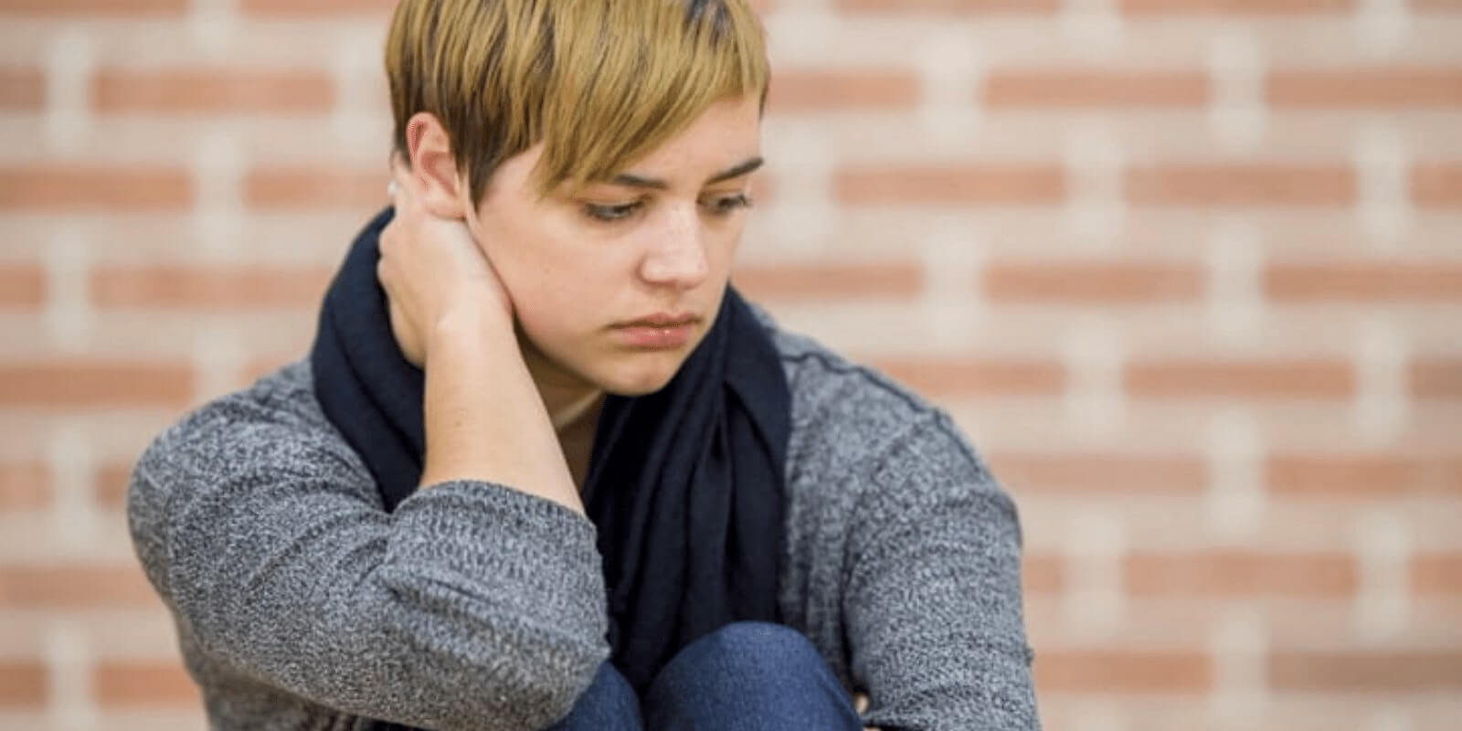 A person looking down while putting her hand behind her neck