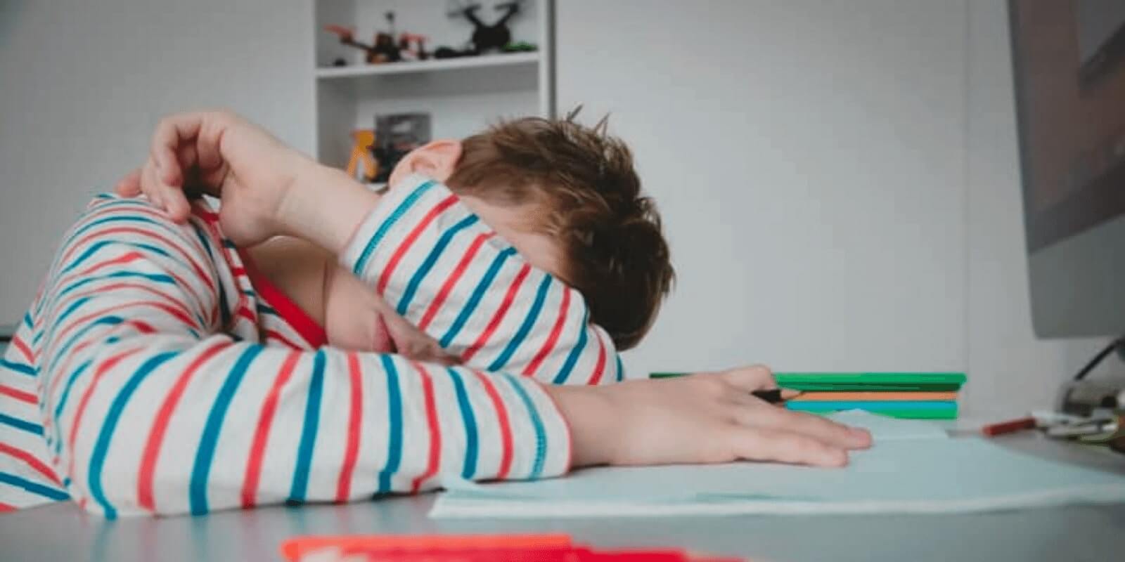 A teen boy putting his head down on a table with his arm crossed