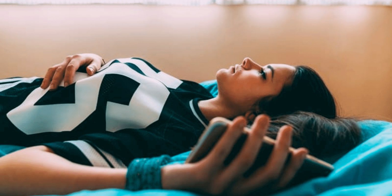 A young female adult laying down on a bed holding her phone
