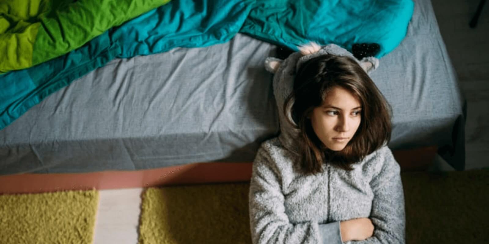 kid sitting on floor with arms crossed leaning against bed