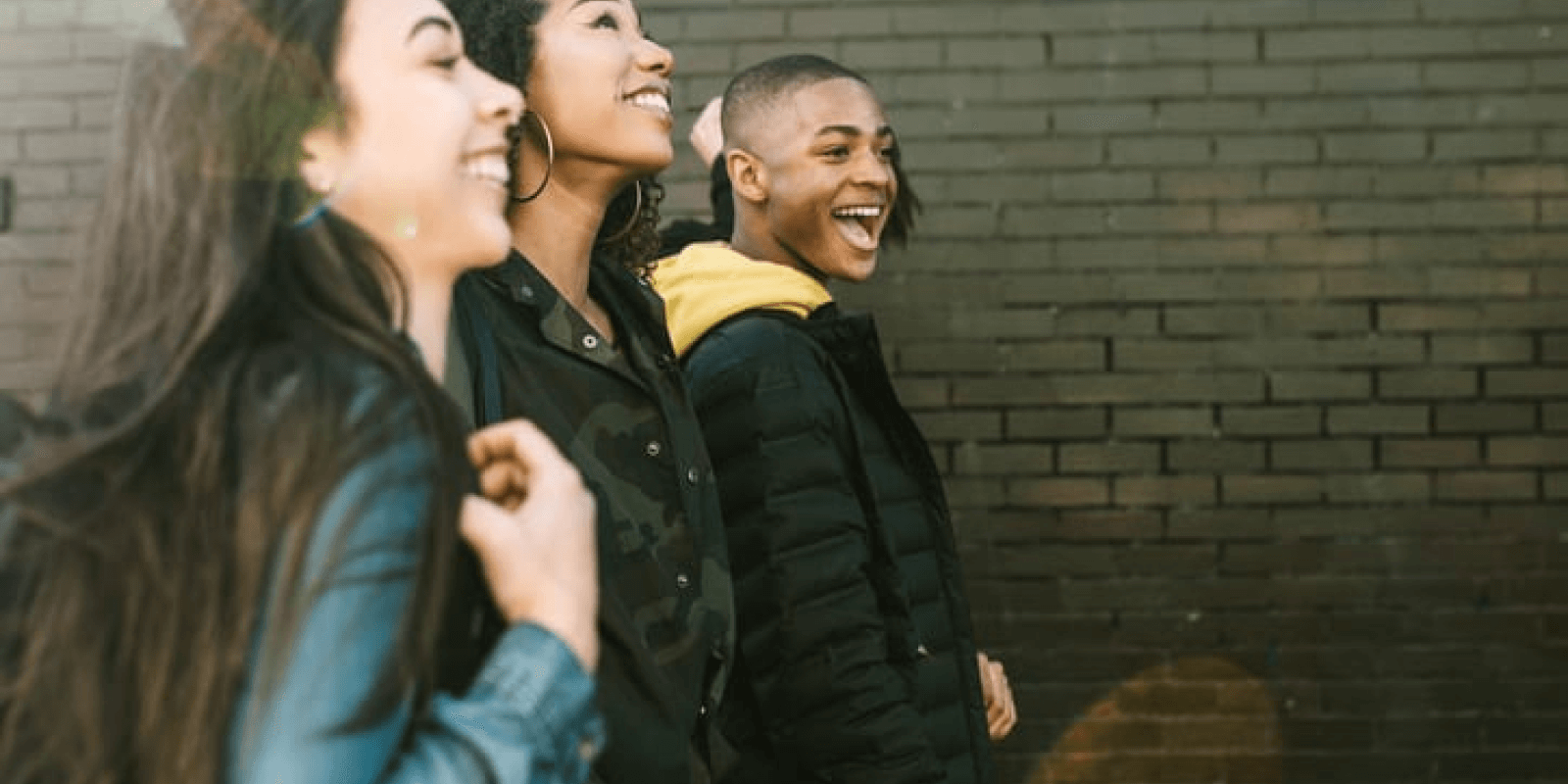 A group of young adults smiling together while they walk along a dark brick wall