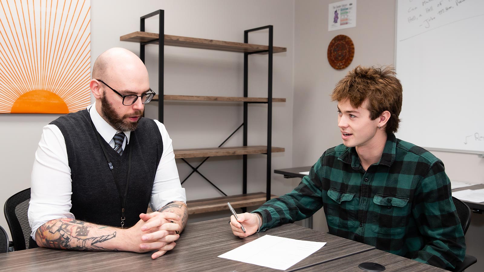 A teacher and young adult engaging in a pleasant conversation in a classroom.