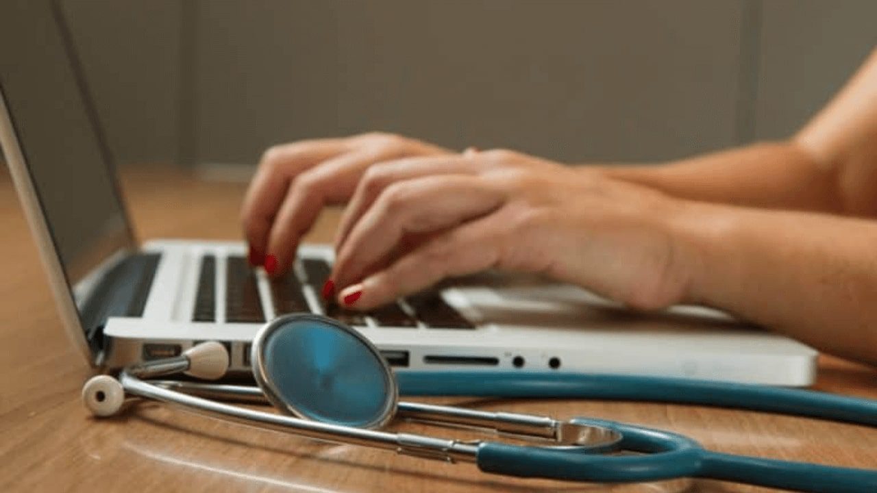 someone is typing on a laptop with a stethoscope on the table