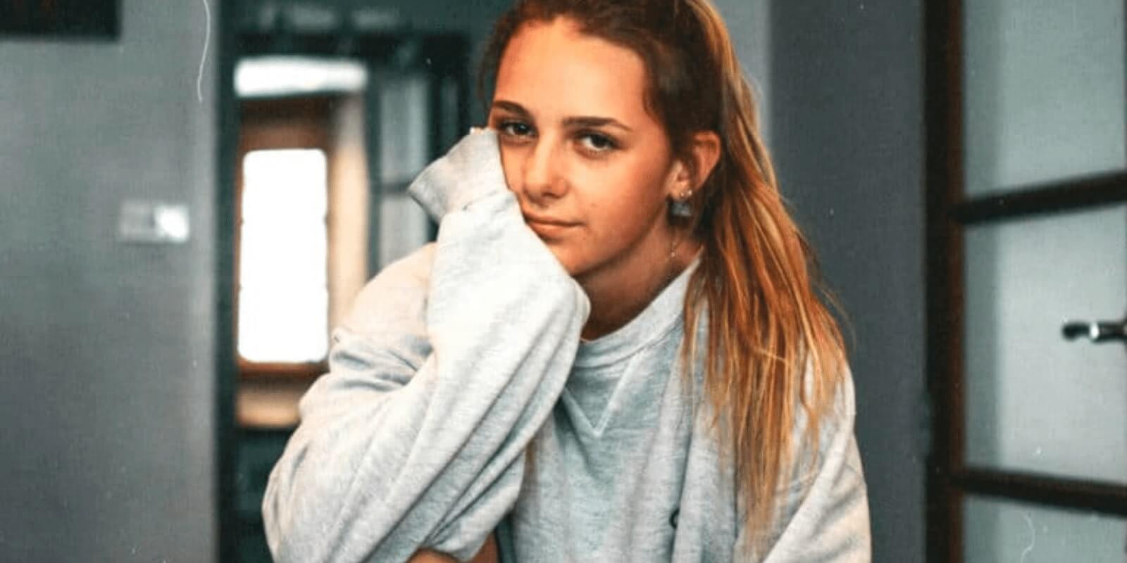 A teenage girl wearing a white sweatshirt leaning her head on her left hand