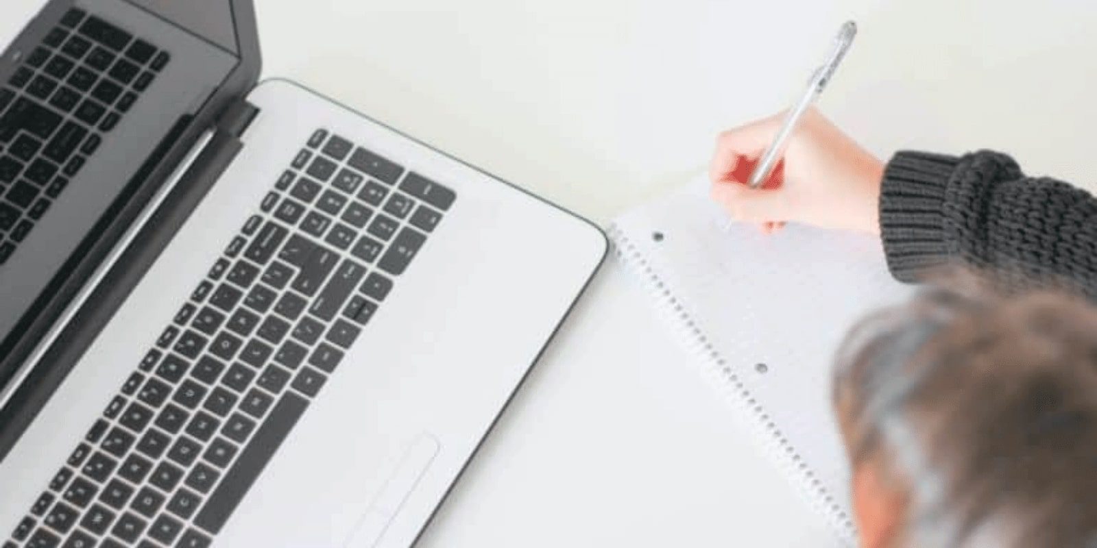 Someone writing notes next to a laptop