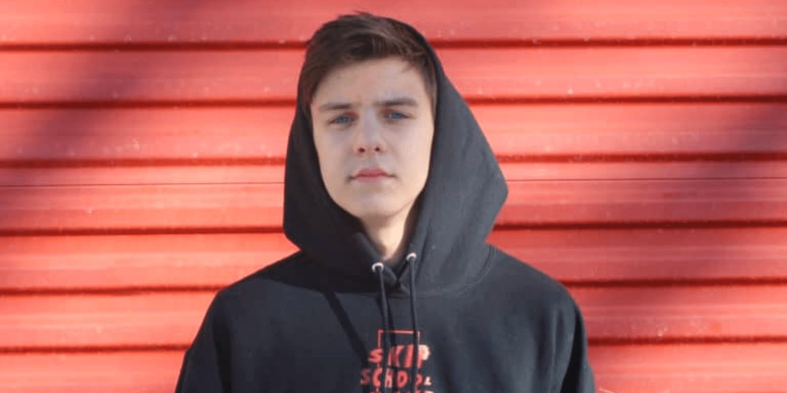 A teen boy wearing a hoodie against red wall