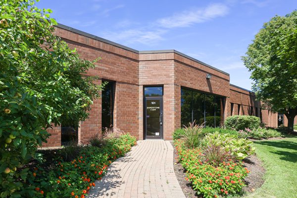 A single-story brick building with landscaped gardens and a brick pathway leading to the entrance.