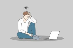 Stress and exhaustion at ideas concept. Young stressed man cartoon character sitting on floor near laptop and feeling frustrated and stuck with ideas vector illustration