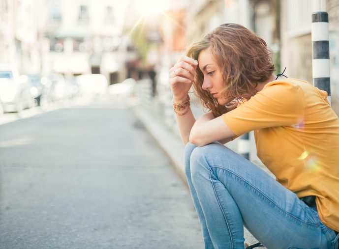 A young woman sitting on the sidewalk facing the street