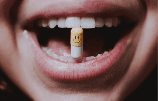 A mouth holding a pill between it's teeth.