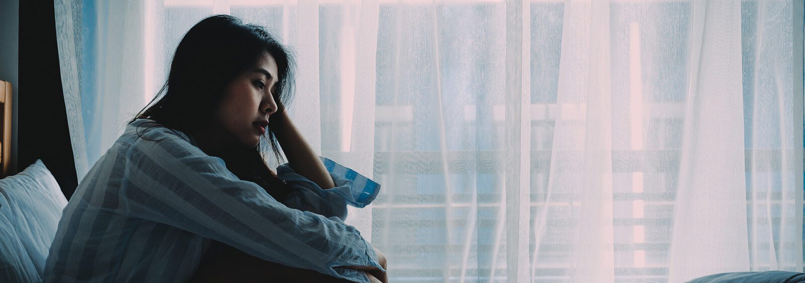 Image of a young woman with her head in her hands sitting up in bed.