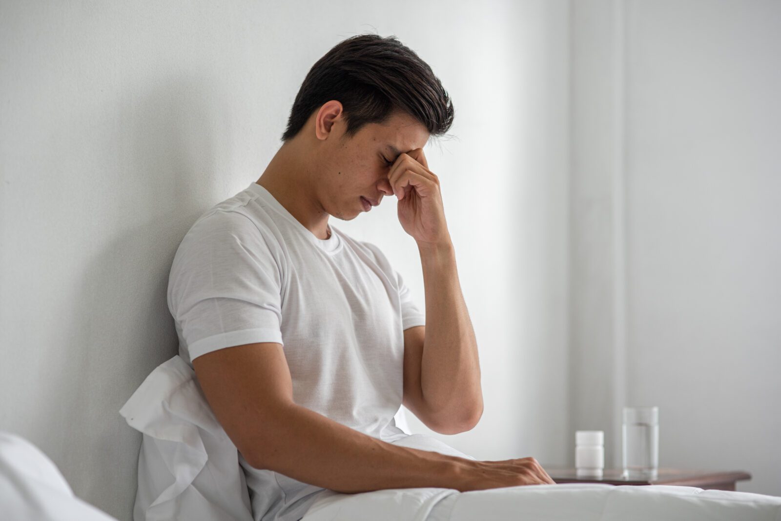 A man squeezing his glabella while sitting on a bed