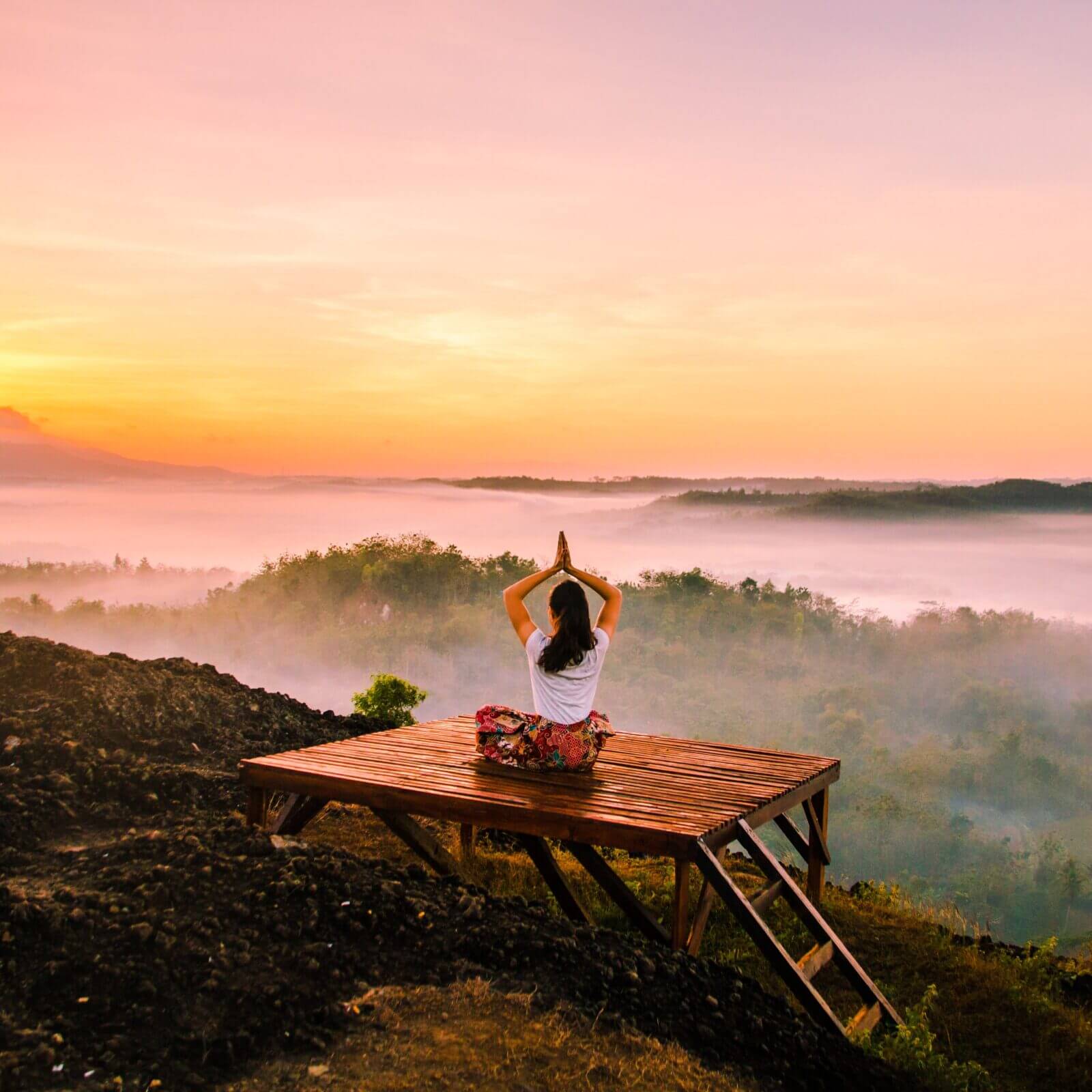 Woman meditating on a platform with a sunset in the background