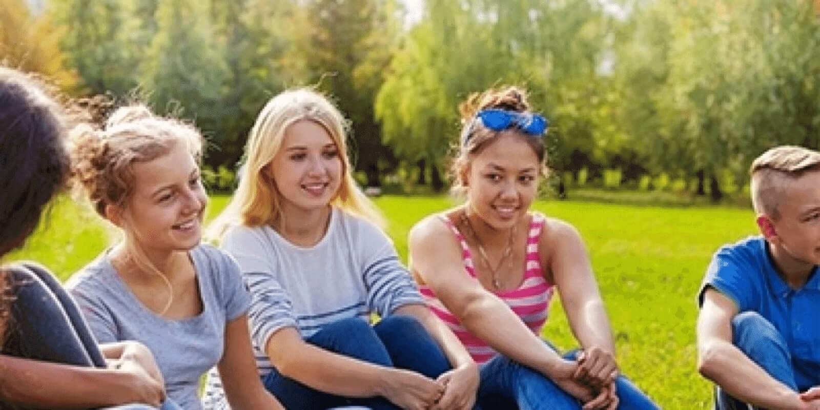 Group of teens sitting on a grassfield smiling at each other