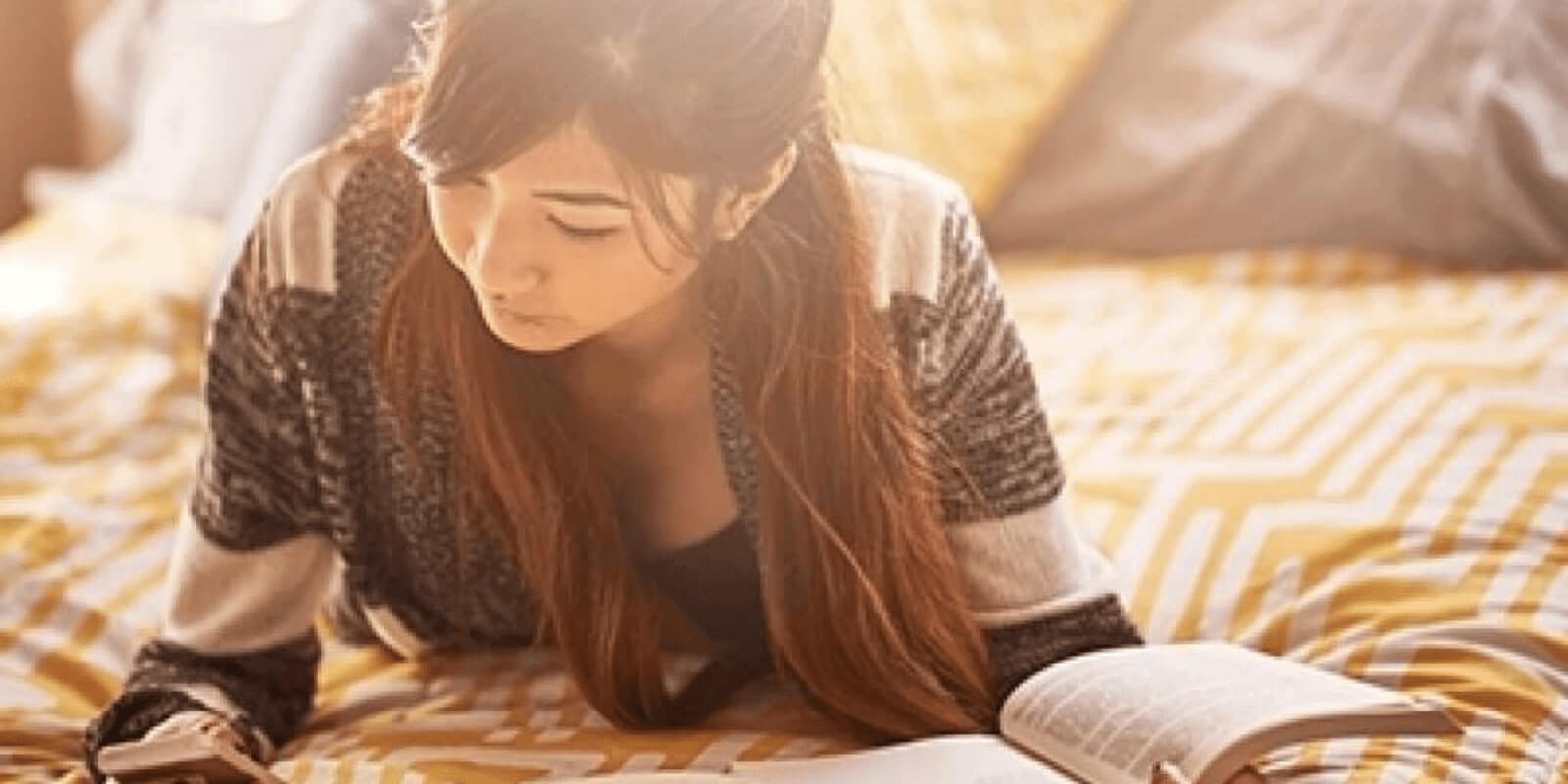 A teen girl holding book while looking at her phone on the bed