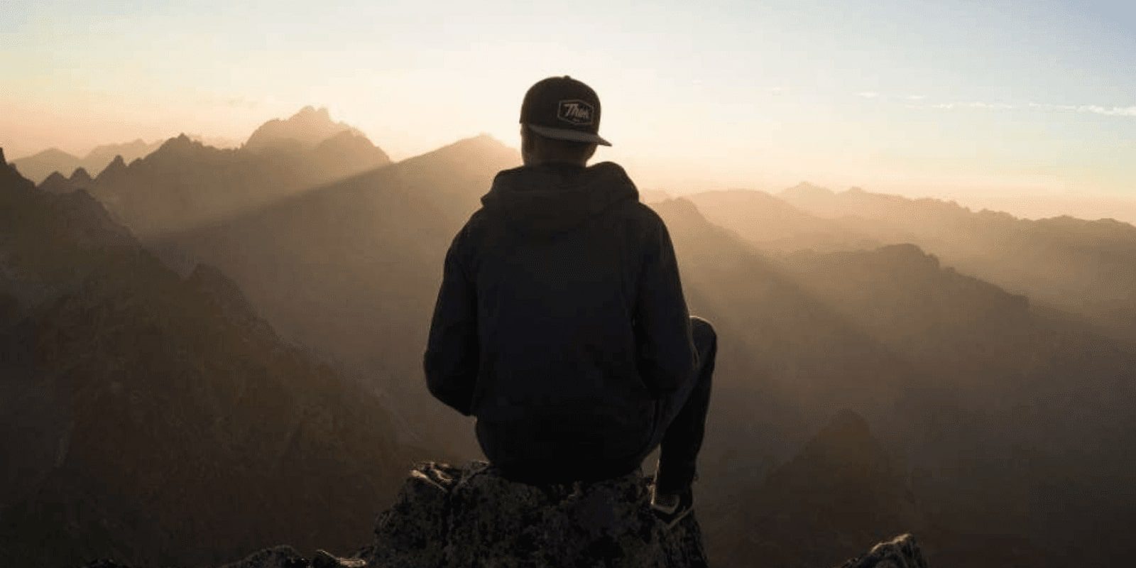 A young man looking at the sunrise in the mountain while sitting on top of the mountain, camera shot from behind