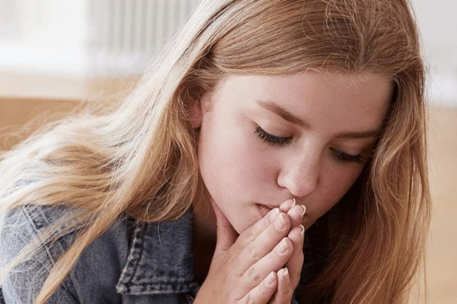 A teenage girl holding hands and putting it below her chin thinking