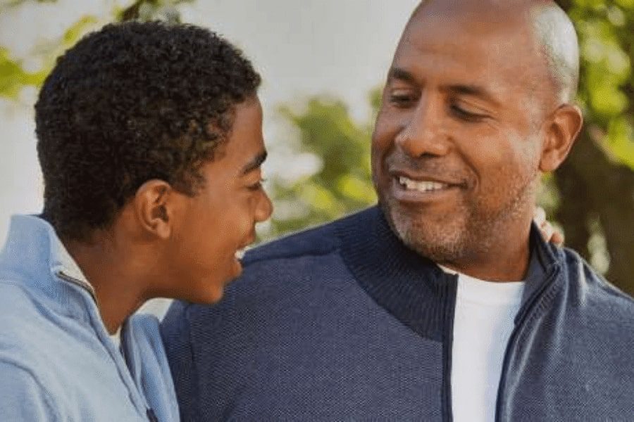 A dad talking and smiling to his son next to him