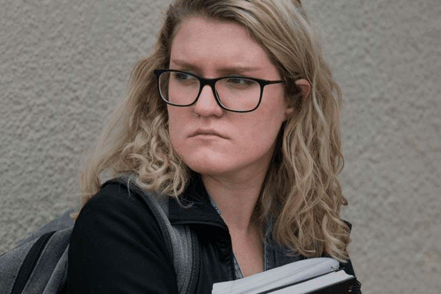 A teen girl with black glasses holding books in her arms looking behind disturbed