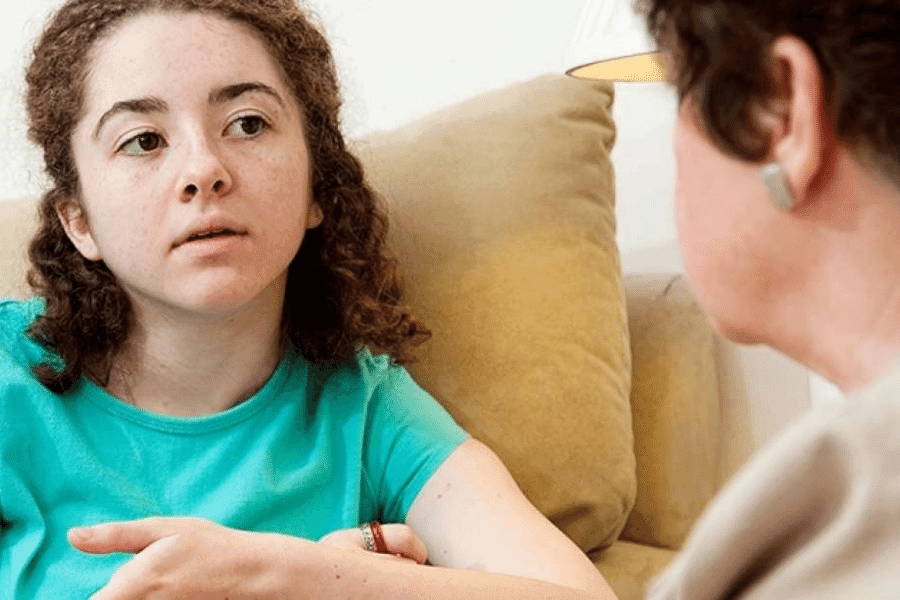 A teen age girl talking to a therapist in a session while sitting on a couch