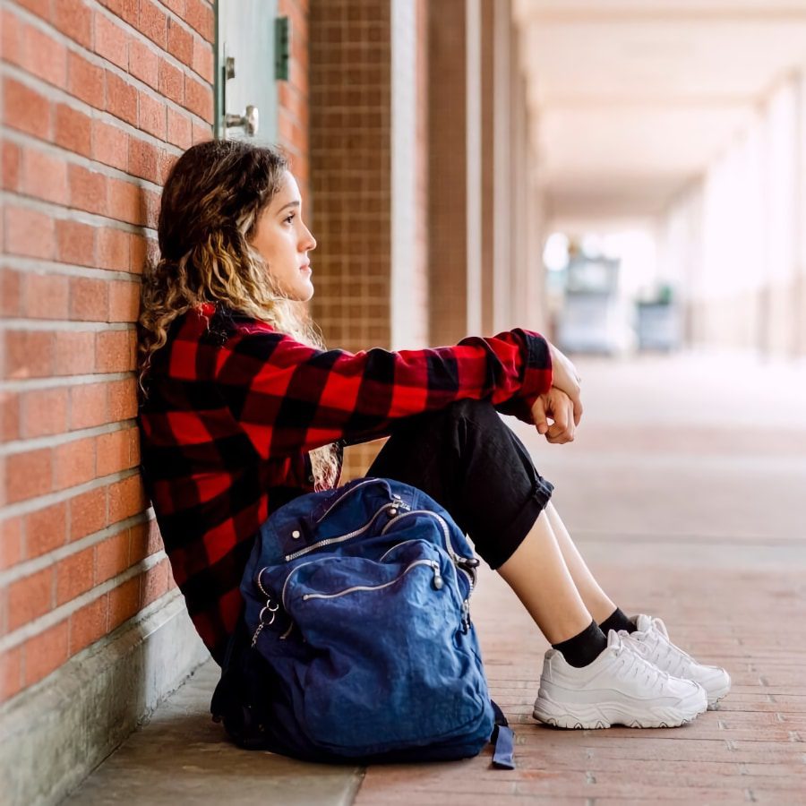 teenage girl sitting against a brick wall
